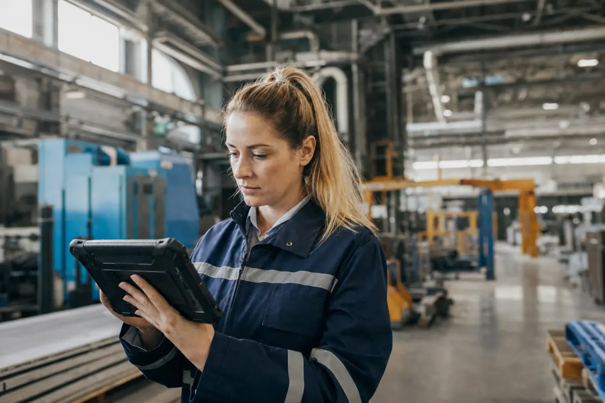 Fachkraft für Arbeitssicherheit prüft eine Meldung auf dem Tablet in der Produktionshalle